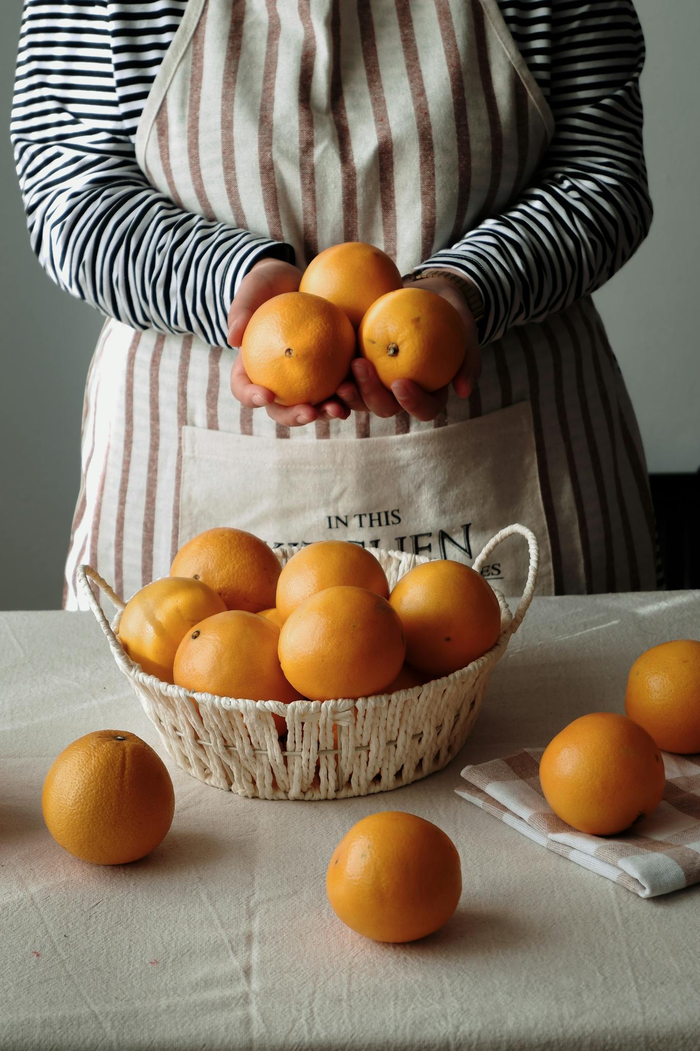 Photo by beytlik A woman holding fresh oranges over a table in a rustic kitchen, showcasing a natural lifestyle.