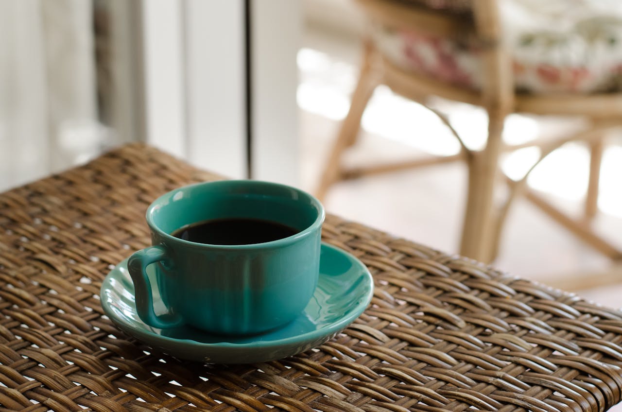 A turquoise coffee cup on a wicker table in a cozy indoor setting.