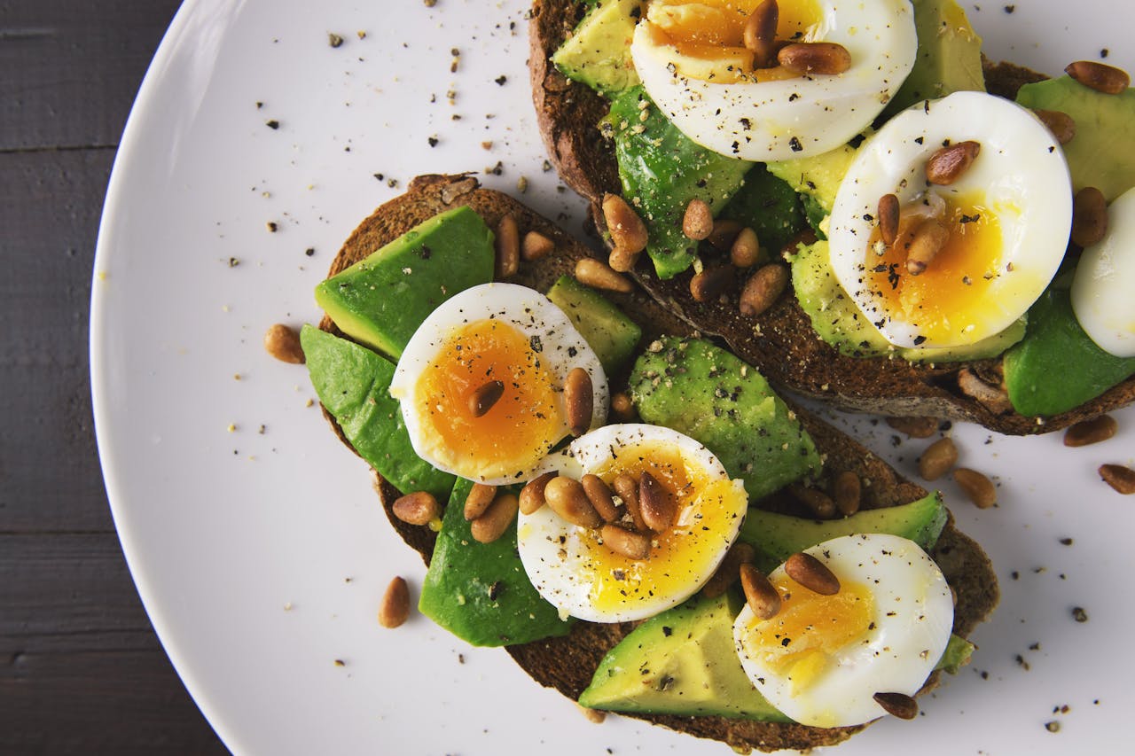 gallery-2 Delicious avocado toast topped with soft-boiled eggs and pine nuts on a white plate.