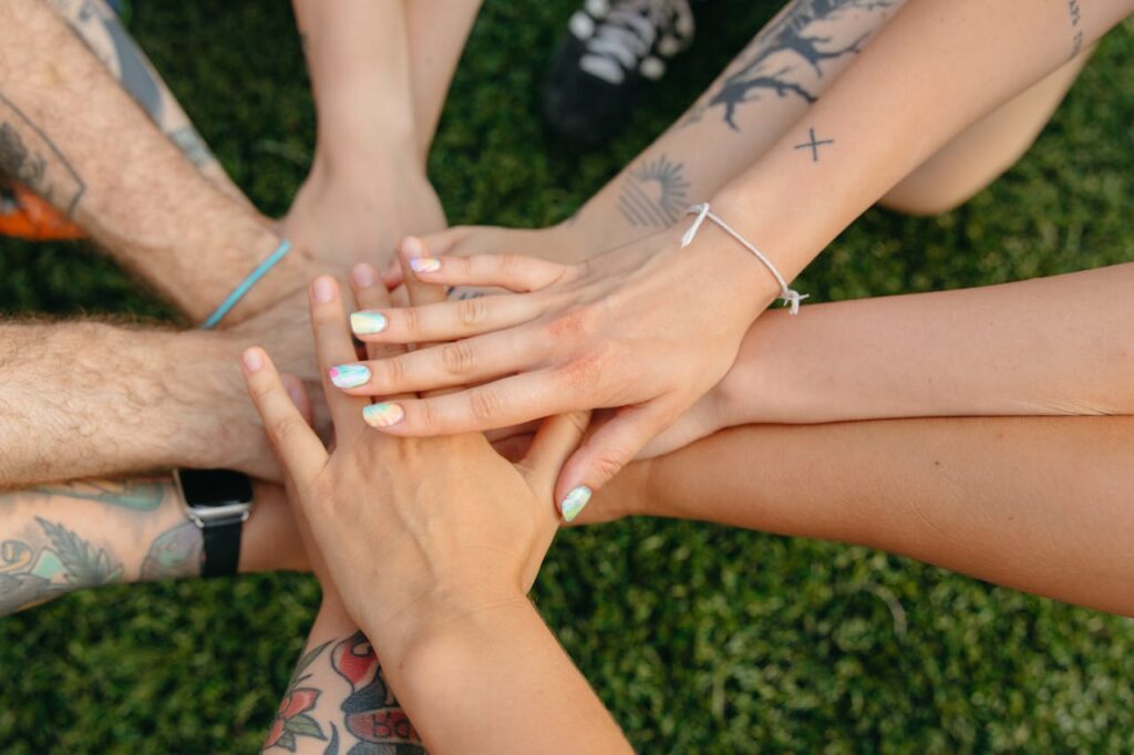 pexels photo 9501978 1 A group of people's hands with tattoos and colorful nails symbolizing unity on grass.